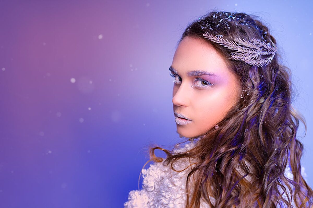 A captivating winter-themed portrait of a woman with snowflakes and icy makeup against a purple background.