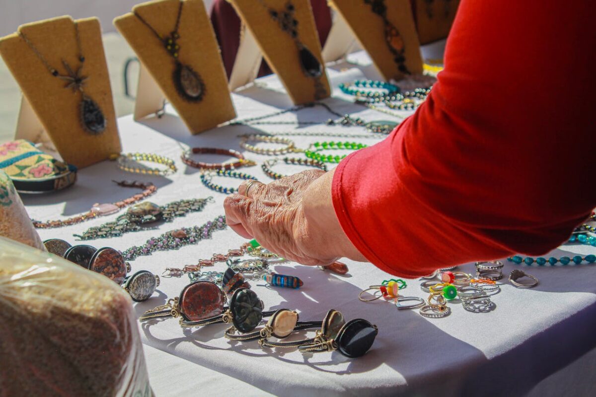 A person shops for handmade jewelry at an outdoor market display.