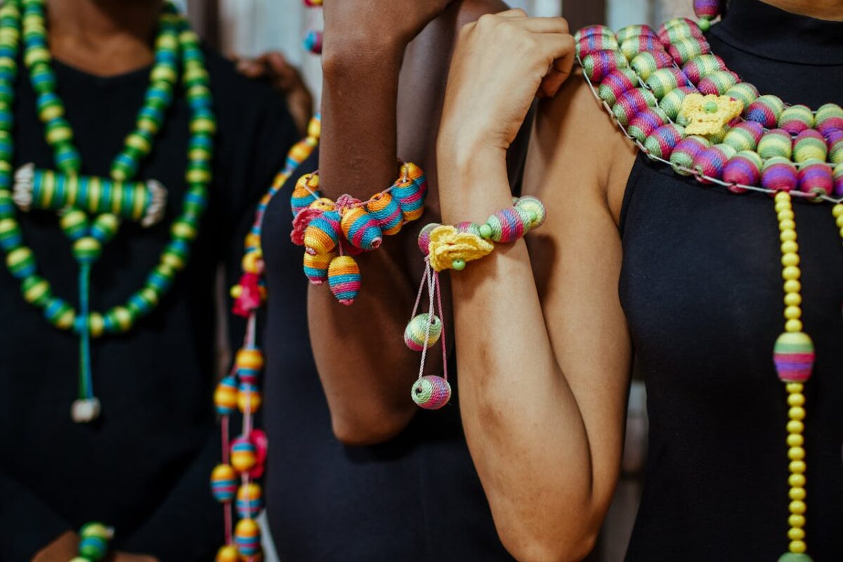 Colorful beaded necklaces and bracelets on diverse individuals wearing black attire.