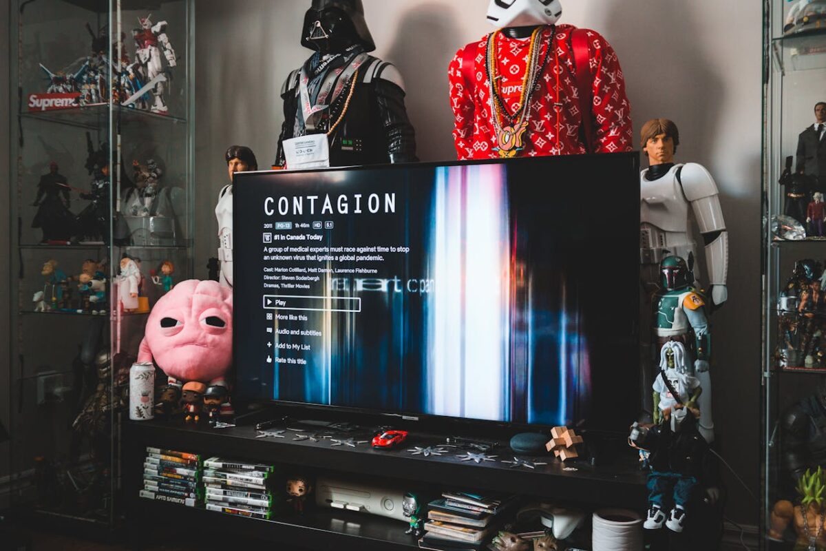 Desktop computer with creative video game on screen near assorted toy superheros on glass shelves in modern style apartment