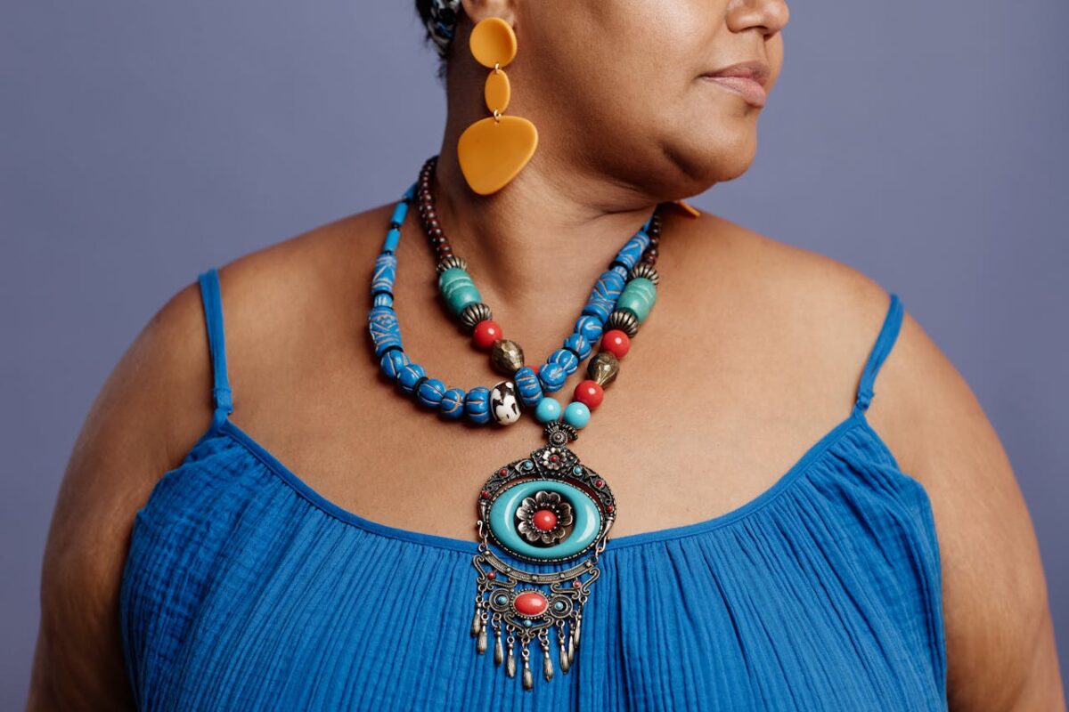 Close-up of a fashionable woman wearing colorful ethnic jewelry and a blue dress on a muted background.