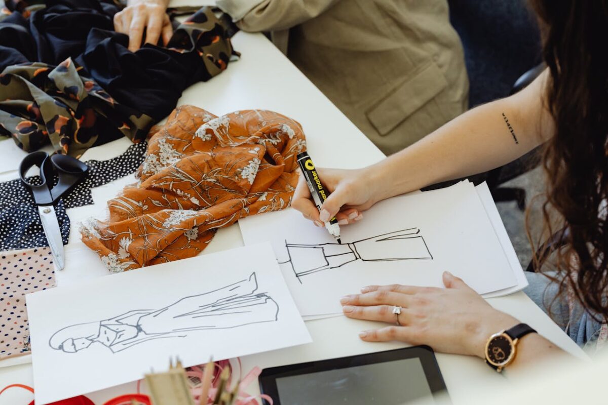 A fashion designer creating clothing sketches surrounded by fabrics and tools.