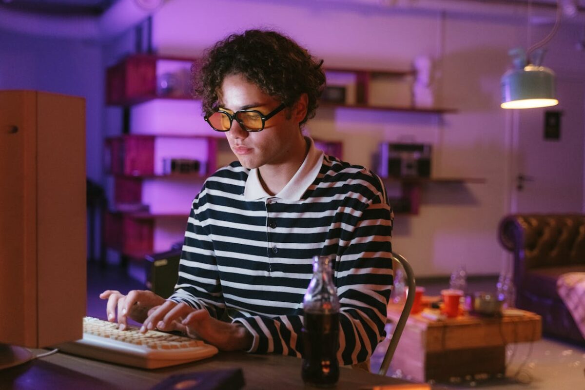 Teenage boy using a retro computer in a cozy room with vibrant lighting, highlighting nostalgic tech vibes.